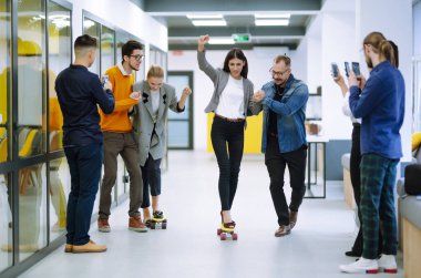 Bir grup iş arkadaşı yaratıcı ofiste kaykayla eğleniyor. Genç meslektaşlarım kaykay yapıyor. Arkadaş canlısı çalışma ekibi pozitif duyguların tadını çıkarıyor.