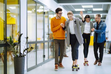 Bir grup iş arkadaşı yaratıcı ofiste kaykayla eğleniyor. Genç meslektaşlarım kaykay yapıyor. Arkadaş canlısı çalışma ekibi pozitif duyguların tadını çıkarıyor.