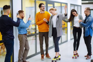 Bir grup iş arkadaşı yaratıcı ofiste kaykayla eğleniyor. Genç meslektaşlarım kaykay yapıyor. Arkadaş canlısı çalışma ekibi pozitif duyguların tadını çıkarıyor.