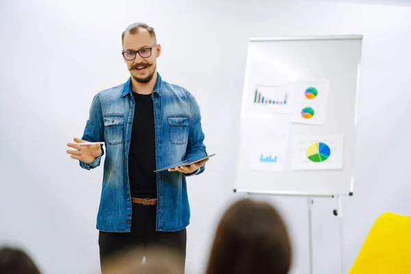 Male business coach speaker giving flipchart presentation. Speaker  having a speech by a whiteboard during a conference business meeting in an office.
