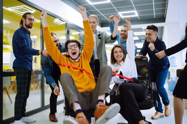 Dost canlısı çalışma ekibi ofis odasında sandalyeye biniyor çeşitli çalışanlar eğlenirken eğleniyor ve eğleniyor yaratıcı çalışanlar birlikte oyun oynuyor..