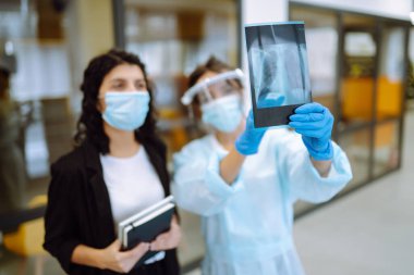 Vizörlü, koruyucu eldivenli genç bir doktor ve röntgen çeken bir hasta. Pnömonia.lşık röntgenleri. Florografi. Covid 2019