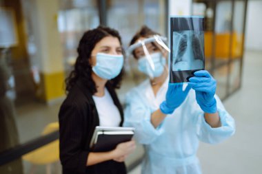 Vizörlü, koruyucu eldivenli genç bir doktor ve röntgen çeken bir hasta. Pnömonia.lşık röntgenleri. Florografi. Covid 2019