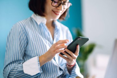 Karantina odasında çalışırken cep telefonu kullanan genç bir kadın. Sosyal ağda arkadaşlarıyla sohbet ediyor, internetten alışveriş yapıyor, telefon kullanarak e-posta yazıyor. Sosyal uzaklık. Kişisel İzolasyon