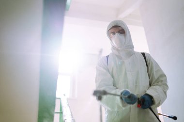 Korunaklı kıyafet giyen bir adam karantina şehrinde koronavirüsün yayılmasını önlemek için sprey kimyasallarla bir apartmanın girişini dezenfekte ediyor. Covid -19. Temizlik kavramı.