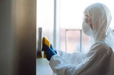 COVID-19 'u önlemek için asansörün temizlenmesi ve dezenfekte edilmesi. Koruyucu giysi giyen işçiler asansörün dezenfektan düğmelerini sıkarlar.. 