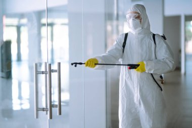 COVID-19 'u önlemek için ofisin dezenfekte edilmesi, karantina şehrinde pandemik olan koronavirüsün yayılmasını önlemek için kimyasal sprey kullanan koruyucu koruyucu koruyucu giysili adam..