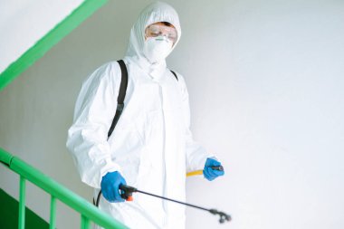 Korunaklı kıyafet giyen bir adam karantina şehrinde koronavirüsün yayılmasını önlemek için sprey kimyasallarla bir apartmanın girişini dezenfekte ediyor. Covid -19. Temizlik kavramı.