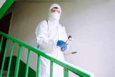 Korunaklı kıyafet giyen bir adam karantina şehrinde koronavirüsün yayılmasını önlemek için sprey kimyasallarla bir apartmanın girişini dezenfekte ediyor. Covid -19. Temizlik kavramı.
