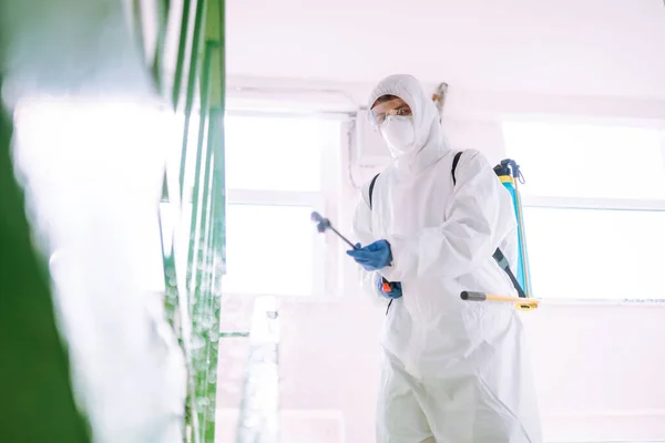 防護服を着た男は コロナウイルスの拡散を防ぐためにスプレー化学物質で住宅の建物の入り口を消毒します Covid 清掃コンセプト — ストック写真