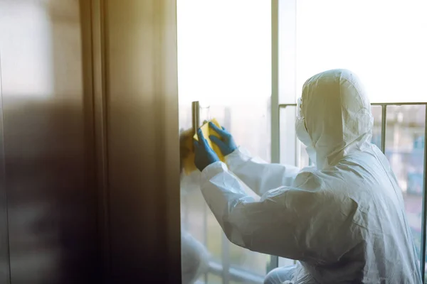 Covid 19を防ぐためにエレベーターの清掃と消毒 防護服を着た労働者がリフトの消毒ボタンをスプレーする — ストック写真
