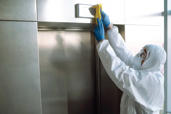 清洗及消毒升降机以防止Covid 穿着防护服的工人在电梯上喷洒消毒剂钮扣 — 图库照片