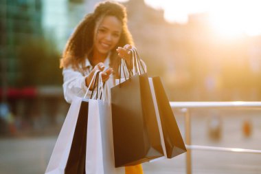 Kadın ellerinde alışveriş torbaları. Alışveriş torbalarıyla sokakta yürüyen genç bir kadın. Bahar atlaması. Tüketim, satış, alım, alışveriş, yaşam tarzı konsepti.
