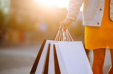 Kadın ellerinde alışveriş torbaları. Alışveriş torbalarıyla sokakta yürüyen genç bir kadın. Bahar atlaması. Tüketim, satış, alım, alışveriş, yaşam tarzı konsepti.