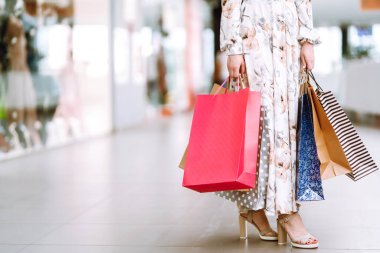 Kadın ellerinde alışveriş torbaları. Alışveriş poşetleriyle alışveriş merkezinde yürüyen genç bir kadın. Bahar alışverişi. Tüketim, satış, alım-satım, yaşam tarzı kavramı.