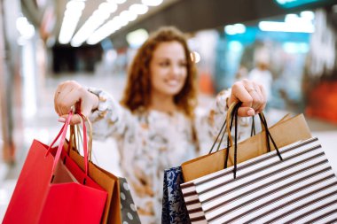 Kadın ellerinde alışveriş torbaları. Alışveriş poşetleriyle alışveriş merkezinde yürüyen genç bir kadın. Bahar alışverişi. Tüketim, satış, alım-satım, yaşam tarzı kavramı.