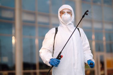 COVID-19 'u önlemek için koruyucu koruyucu koruyucu koruyucu koruyucu giysili bir adam koronavirüsün yayılmasını önlemek için sprey kimyasallarla dezenfekte ediyor. Temizlik kavramı.