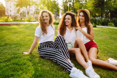 Üç genç kadın çimlerin üzerinde dinleniyor. Genç arkadaşlar birlikte gülüyor ve tatilin tadını çıkarıyorlar. Arkadaşlık, gençlik ve seyahat kavramı.