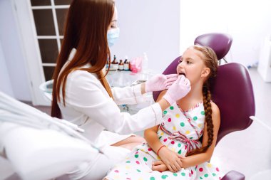 Küçük kız dişçiyi ziyaret ediyor. Dişçinin dişlerini tedavi ederken ağzını kocaman açan güzel bir kız. Erken önleme, ağız hijyeni ve süt diş bakımı.