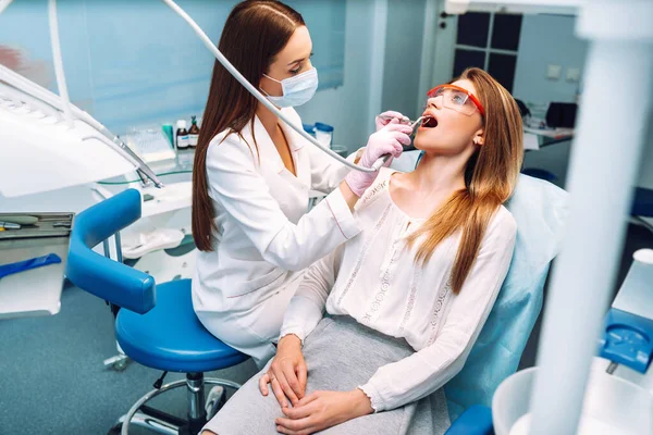 歯医者に歯を治療中に口を大きく開けた若い女性 患者の口の近くに歯科機器を保持する医師の手 健康な歯と薬の概念 — ストック写真