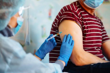 Doktor yaşlı hastayı evde aşılıyor. Tıbbi maskeli hastaya iğne yapmadan önce elinde şırınga olan ve pamuk kullanan doktoru kapat. Covid-19 koronavirüs aşısı, grip, bulaşıcı hastalıklar.