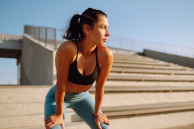 Spor kıyafetli genç bir kadın sabahları dışarıda egzersiz yapıyor. Yoğun bir antrenmandan önce kaslarını ısıtıyorum. Spor, aktif yaşam, spor eğitimi, sağlıklı yaşam tarzı..