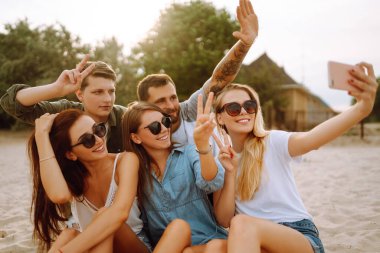 Sahilde telefonla selfie çeken bir grup insan. Genç arkadaşlar birlikte yaz partisinin tadını çıkarırlar. İnsanlar, yaşam tarzı, seyahat, doğa ve tatil kavramı.