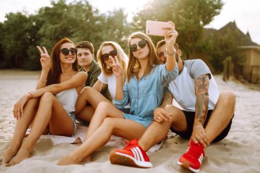 Sahilde telefonla selfie çeken bir grup insan. Genç arkadaşlar birlikte yaz partisinin tadını çıkarırlar. İnsanlar, yaşam tarzı, seyahat, doğa ve tatil kavramı.