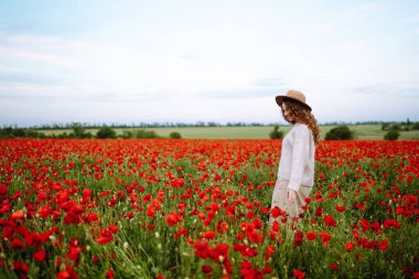 Harika bir haşhaş tarlasında yürüyen genç bir kadın. Yaz zamanı. Gelincik tarlasında poz veren güzel bir kadın. Doğa, tatil, rahatlama ve yaşam tarzı.