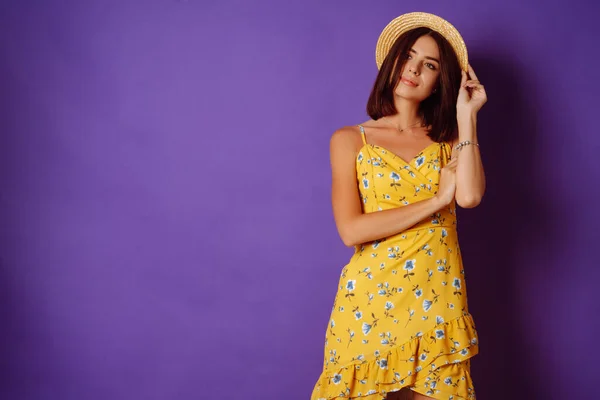 Smiling woman in yellow dress and hat posing purple background. Fashion, style, summer concept.