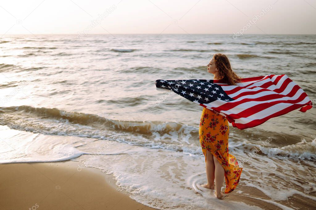 Young woman with american flag on the beach at sunset. 4th of July. Independence Day. Patriotic holiday.