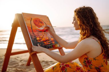 Güzel kadın ressam, kumsalda yağlı renklerle resmini tuvale çiziyor. Sanat, yaratıcılık ve ilham kavramı.