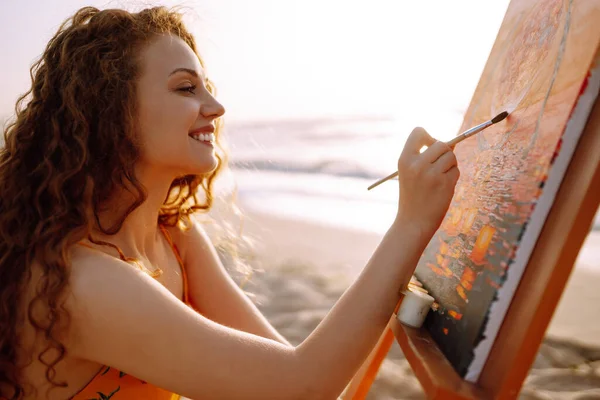 Beautiful woman artist drawing her picture on canvas with oil colors at the beach. Art, creativity and inspiration concept.