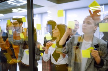 İş arkadaşları cam duvara yapışkan bir not yazıyorlar ve iş arkadaşları ofiste bekliyor. Takım çalışmasında planlama, analiz, işbirliği. 