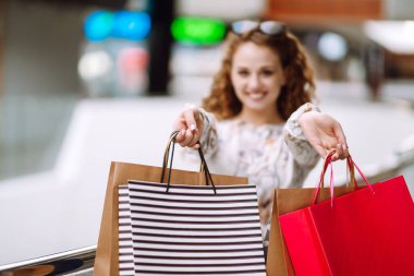 Alışveriş poşetleriyle alışveriş yaptıktan sonra alışveriş merkezinde yürüyen genç bir kadın. Tüketim, satış, alım, alışveriş, yaşam tarzı konsepti.