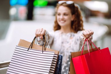Alışveriş poşetleriyle alışveriş yaptıktan sonra alışveriş merkezinde yürüyen genç bir kadın. Tüketim, satış, alım, alışveriş, yaşam tarzı konsepti.