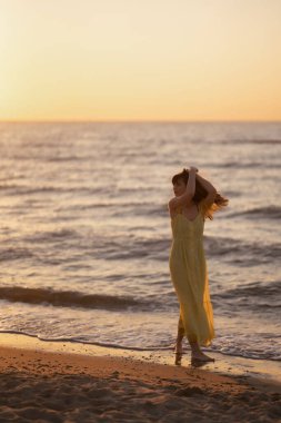 Genç bir kadın sahilde günbatımının tadını çıkarıyor. Kadınsı, çekici ve şehvetli bir siluet. Seyahat, hafta sonu, rahatlama ve yaşam tarzı konsepti.