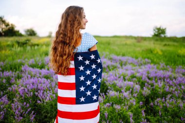 Mutlu kadın Amerika bayrağıyla dışarıda çiçek açan çayırda poz veriyor. 4 Temmuz. Bağımsızlık Günü. Vatansever bayram.