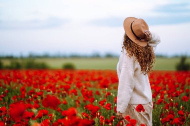 Arkadan bak. Şapkalı genç kıvırcık kadın haşhaş tarlasında poz veriyor. Doğa, tatil, rahatlama ve yaşam tarzı. Yaz manzarası.