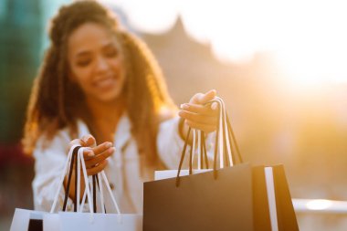 Kadın ellerinde alışveriş torbaları. Alışveriş torbalarıyla sokakta yürüyen genç bir kadın. Tüketim, satış, alım-satım, yaşam tarzı kavramı.