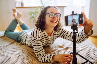 Genç bir kadın video blogunu kaydediyor. Kadın blogcu video bloğunu evde kaydediyor. Vlogger telefon kullanarak çevrimiçi yayın yapıyor. Sosyal medya, instagram, evde kalıp karantina.