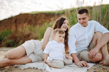 Kumsalda genç bir aile. İnsanlar yaz tatilinde eğleniyorlar. Baba, anne ve çocuk mavi denizin ve gökyüzünün arka planına karşı. Seyahat, aktif yaşam tarzı, tatil, dinlenme konsepti.