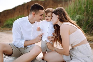 Kumsalda genç bir aile. İnsanlar yaz tatilinde eğleniyorlar. Baba, anne ve çocuk mavi denizin ve gökyüzünün arka planına karşı. Seyahat, aktif yaşam tarzı, tatil, dinlenme konsepti.