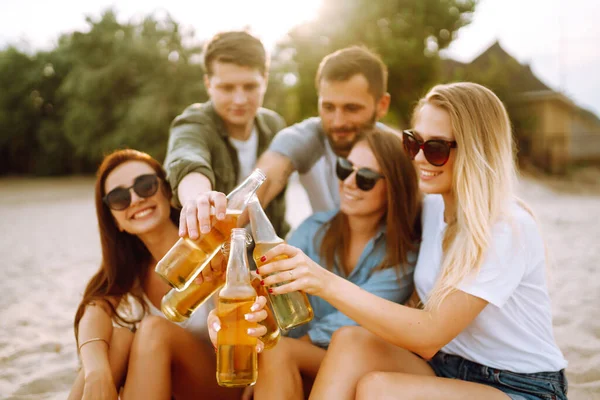 The young friends holding bottles with beer at the beach party. Group of friends having fun, relaxing, toasting with beerus. People, lifestyle, travel, nature and vacations concept.