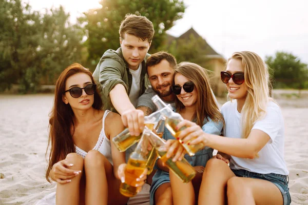 The young friends holding bottles with beer at the beach party. Group of friends having fun, relaxing, toasting with beerus. People, lifestyle, travel, nature and vacations concept.