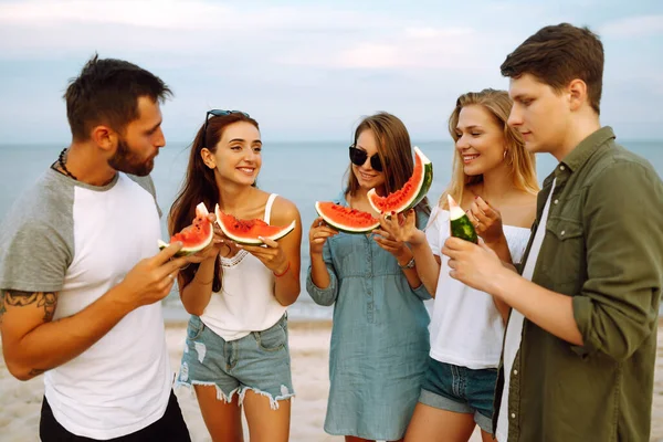 ピクニックをしたり スイカを食べたり ビーチで夏のパーティーを楽しむ若い友人のグループ 幸せな友人が一緒に海の近くに座って休んでいる ビーチホリデーと夏休みのコンセプト — ストック写真