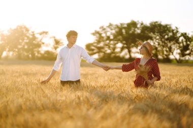Genç mutlu çift gün batımında buğday tarlasında sarılıyor. Birlikte eğleniyoruz. Gençlik, aşk ve yaşam tarzı kavramı.