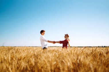 Genç mutlu çift gün batımında buğday tarlasında sarılıyor. Birlikte eğleniyoruz. Gençlik, aşk ve yaşam tarzı kavramı.