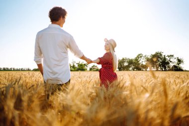 Genç mutlu çift gün batımında buğday tarlasında sarılıyor. Birlikte eğleniyoruz. Gençlik, aşk ve yaşam tarzı kavramı.
