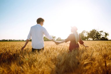 Genç mutlu çift gün batımında buğday tarlasında sarılıyor. Birlikte eğleniyoruz. Gençlik, aşk ve yaşam tarzı kavramı.